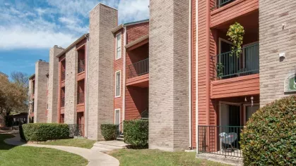 A row of modern red and beige apartment buildings with spacious balconies surrounded by green landscaping.