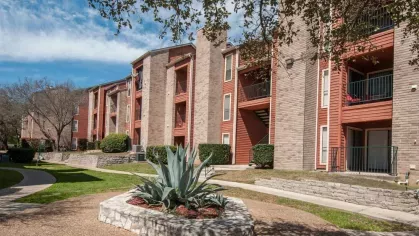 A landscaped courtyard with a large agave plant centerpiece, surrounded by red and beige apartment buildings.