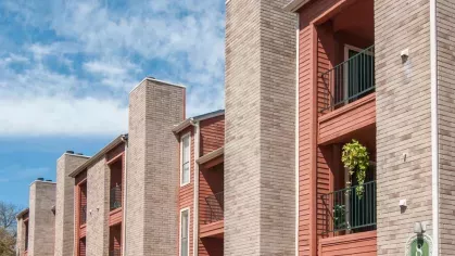 A side angle of multi-level apartment buildings with spacious balconies, framed by a bright blue sky.