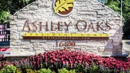 A close-up of the Ashley Oaks Apartment Homes sign, framed by vibrant flowers and greenery.
