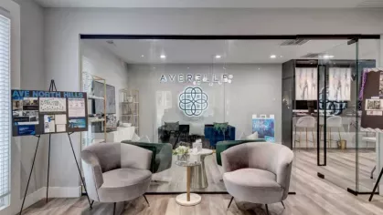 A welcoming leasing office with stylish gray chairs, a small table, and a glass door showcasing the Averelle North Hills logo inside.