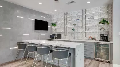 A chic entertainment area featuring a marble-top bar with high-back chairs, open shelving, and a flat-screen TV, ideal for socializing.