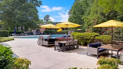 A resort-style pool area with patio seating, umbrellas, and landscaping, perfect for outdoor leisure.