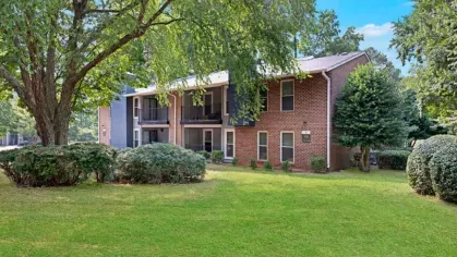 A well-maintained brick apartment building with balconies and lush green landscaping.