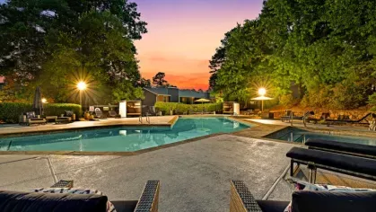 A sparkling swimming pool illuminated at sunset, surrounded by lounge chairs, trees, and a peaceful atmosphere.