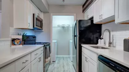 A bright kitchen with stainless steel appliances, white cabinetry, and a view of a pantry and laundry area, creating a functional and modern space.