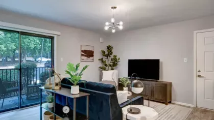 A cozy living room with a comfortable sofa, modern decor, and a large sliding glass door leading to a private balcony with greenery in the background.
