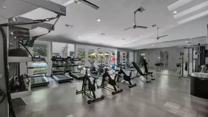 A spacious fitness center with treadmills, exercise bikes, weight machines, and floor-to-ceiling windows offering a view of the pool area.