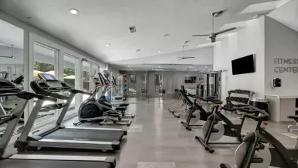 A fully equipped fitness center with modern exercise equipment, including stationary bikes and treadmills, in a well-lit space with high ceilings.