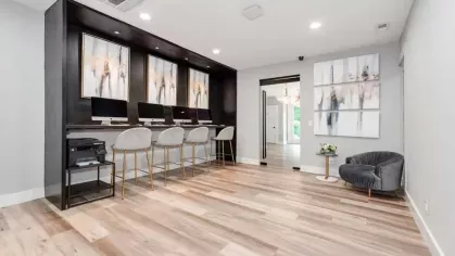 A sleek business center with a row of computers, barstool seating, and contemporary artwork on a dark accent wall.