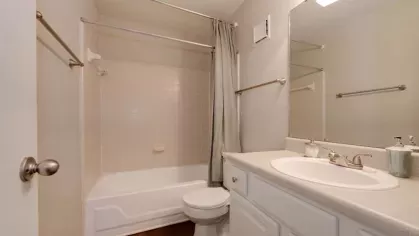 A bright and clean bathroom featuring a bathtub with a shower, white vanity, and a large mirror with modern lighting.