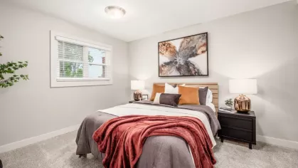 Another angle of a warm and inviting bedroom showcasing a neatly made bed with layered pillows and a red throw, accentuated by a large window and soft lighting.