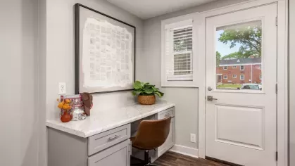 A stylish built-in desk area with marble-like countertops, a comfortable chair, and a view of a window and door leading outside.