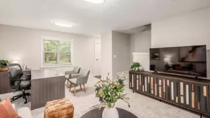 A spacious living area with an open concept, combining a TV space, home office desk, and natural light from a large window.