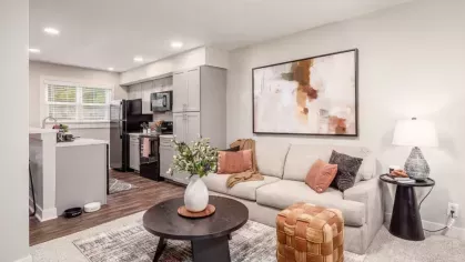 A cozy living room with a beige sectional sofa, decorative pillows, a round coffee table, and modern artwork on the wall.