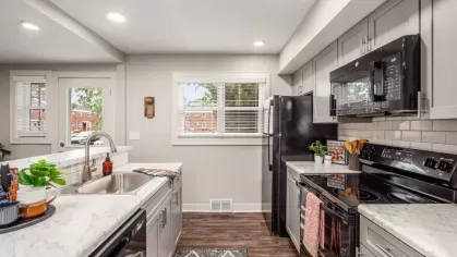 A modern kitchen with marble countertops, black appliances, and a large window providing natural light.