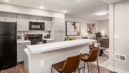 A contemporary kitchen with a breakfast bar, high stools, and sleek cabinetry connecting to a living area.