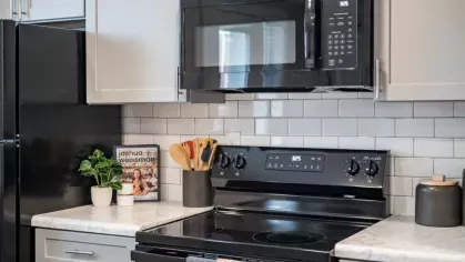 A close-up view of a modern stove with a black microwave and subway tile backsplash.