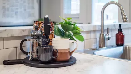 A stylish coffee station on a kitchen counter, featuring mugs, a French press, and greenery.