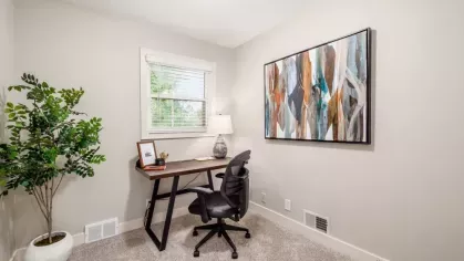 A bright home office with a small desk, ergonomic chair, potted plant, and colorful abstract artwork on the wall.