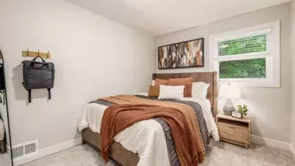 A serene bedroom with a plush bed, earthy-toned bedding, and a large abstract painting on the wall.