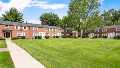 A wide view of Bexley Plaza apartments showing neatly maintained red-brick buildings and lush green lawns under a clear blue sky.