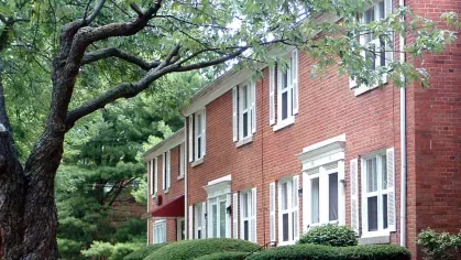 Close-up of red-brick apartment buildings at Bexley Plaza, surrounded by well-manicured shrubs and trees.