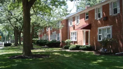 A row of red-brick apartment buildings at Bexley Plaza with a tree-lined walkway and neatly trimmed landscaping.