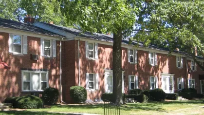 A side view of red-brick Bexley Plaza apartments featuring large trees providing shade over the lawn and walkway.