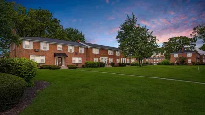 A serene view of a brick apartment complex at twilight with manicured lawns and vibrant sky hues.
