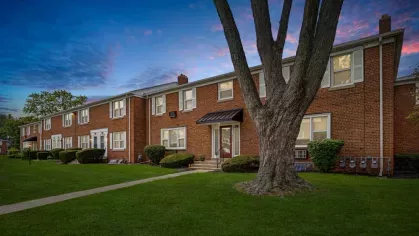 A close-up of a tree framing a brick apartment building with a peaceful twilight sky.