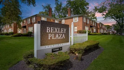 The Bexley Plaza sign prominently displayed in front of a manicured lawn and brick apartment complex at twilight.