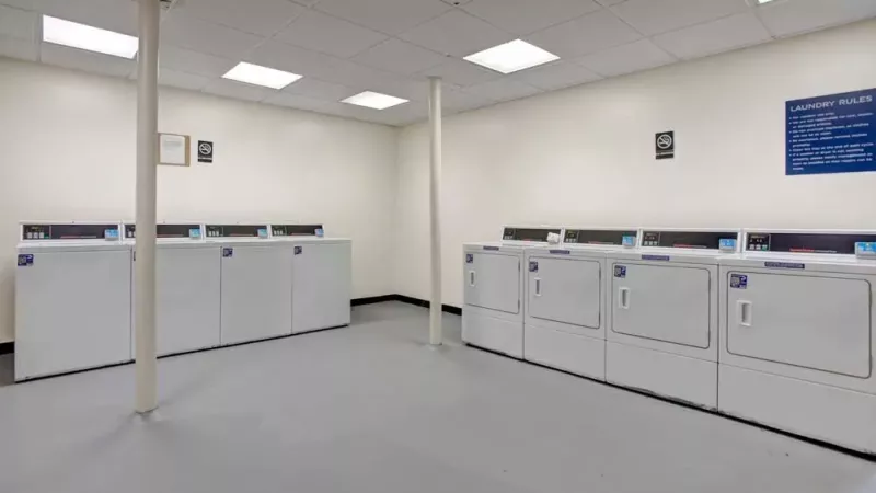 A modern laundry room with multiple washers and dryers lined against the wall under bright lighting.
