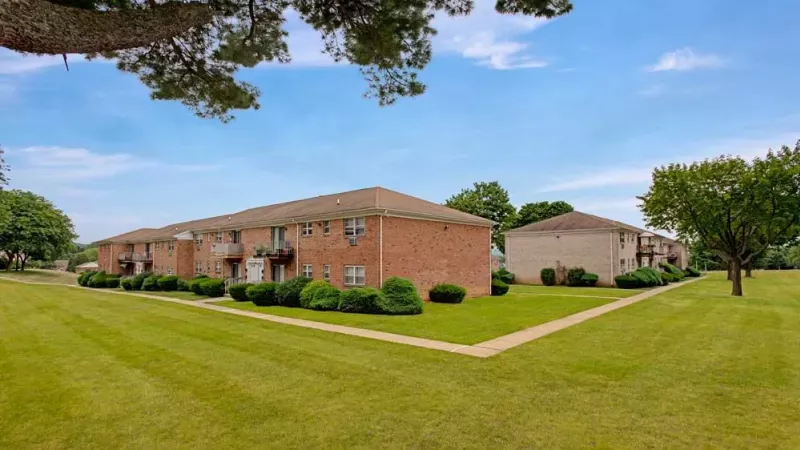 A wide view of brick apartment buildings surrounded by neatly maintained lawns and walkways under a clear blue sky.