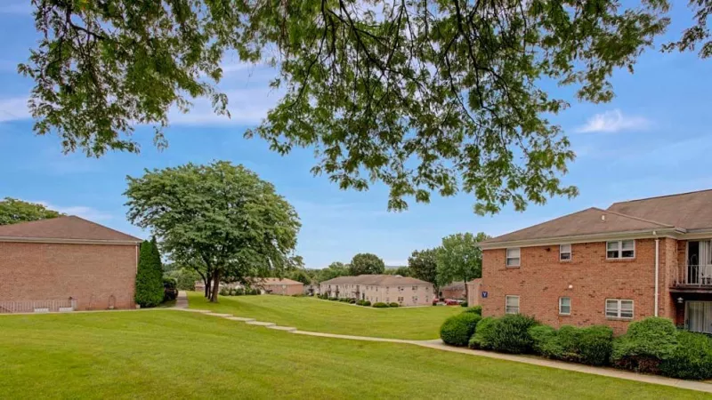 A peaceful outdoor view of grassy lawns and multiple apartment buildings framed by trees.