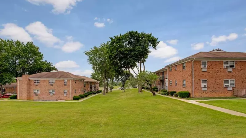 A walkway leading between two rows of red-brick apartment buildings with vibrant green grass and trees.
