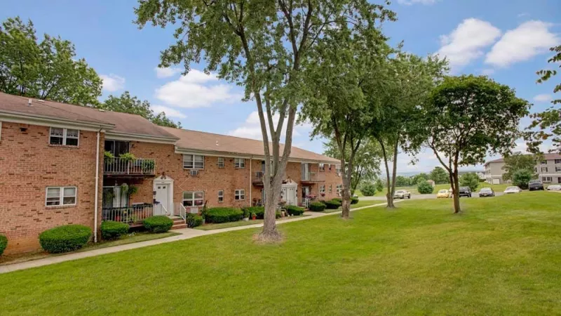 A closer view of red-brick apartments with balconies and shrubbery in a landscaped setting.