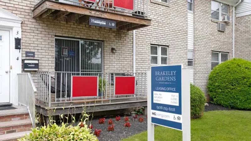 A wide-angle view showcasing brick apartment buildings with landscaped gardens and a bright blue sky above.
