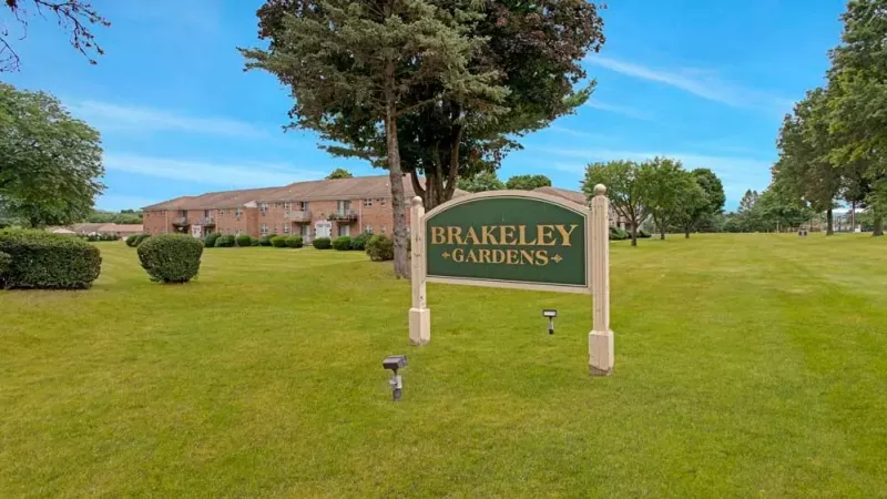 A close-up of a beige brick apartment complex with manicured landscaping and red accents.