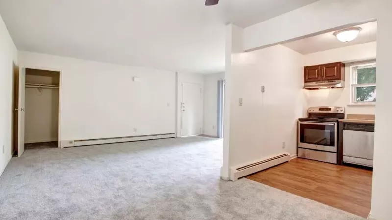 A bright living room with sliding glass doors, a gray carpet, and a ceiling fan, offering ample space for furniture and decor.