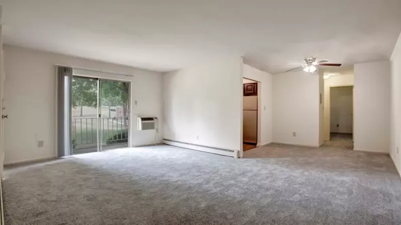 A simple bedroom with a large window, gray carpet, and white walls, providing a blank canvas for personalization.