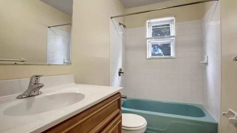 A clean bathroom featuring a white vanity, a blue bathtub, and a window providing natural light.