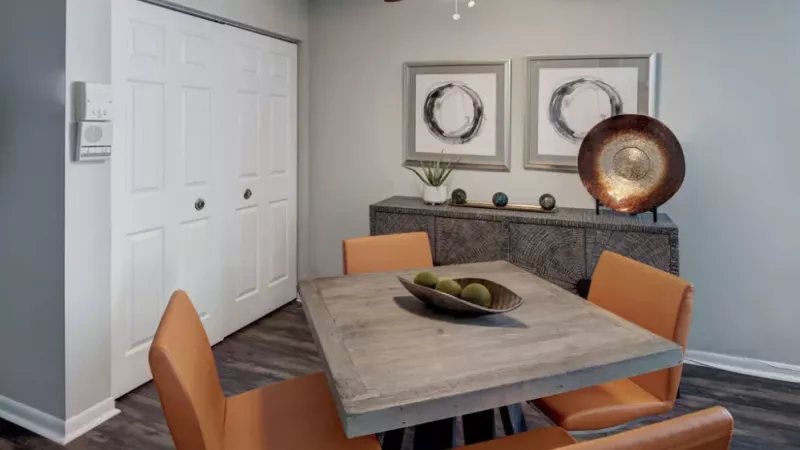 A cozy dining area featuring a wooden table, orange chairs, and modern artwork on the wall.