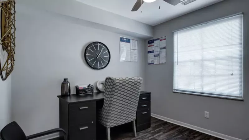 A compact workspace with a sleek black desk, a patterned chair, and a wall clock.