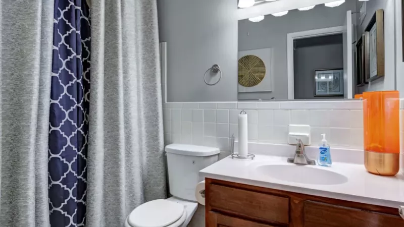 A bathroom with a tiled wall, wooden cabinets, and a navy blue patterned shower curtain.