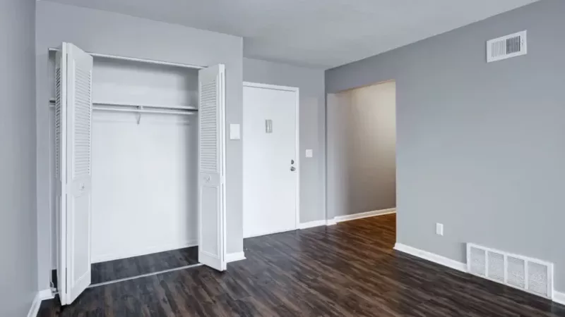 A living area with hardwood flooring, an open closet, and a view of the entryway door.