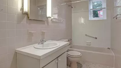 A tiled bathroom with a vanity sink, toilet, bathtub, and a window for natural light.