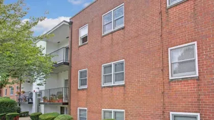 A corner view of a red brick apartment building with well-maintained bushes.