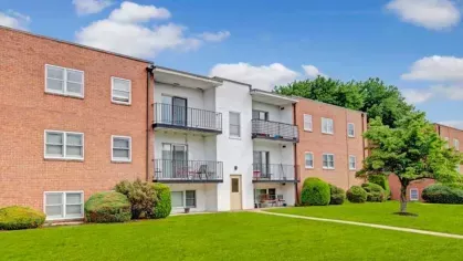 A red brick apartment building with white accents and a central pathway cutting through a green lawn.