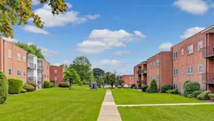 A broad view of a landscaped courtyard with a pathway surrounded by two rows of brick apartment buildings.